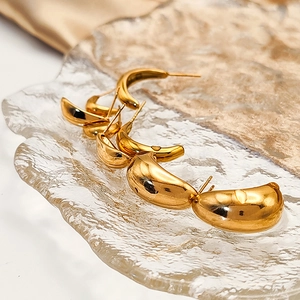 Macro detail of three pairs of golden teardrop stud earrings on a textured glass tray