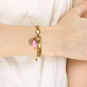 Close-up of golden link bracelet with pink heart and rhinestone flower charms on a wrist