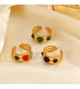 Detailed view of three 18K gold-plated rings with colorful resin stones on beige silk fabric