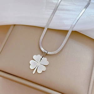 Detailed close-up of silver clover pendant on flat snake chain over beige jewelry box
