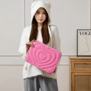 Detail of pink quilted heart pattern laptop sleeve held by a model in a cozy setting
