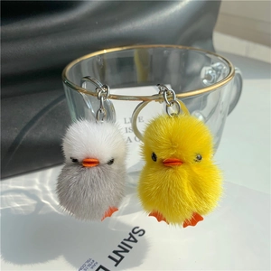 Close-up of yellow and white plush duck keychains hanging on a glass cup rim