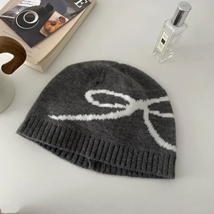 Flat lay of a grey knitted beanie with white bow pattern on a stylish white desk setup