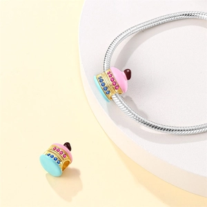 Macro detail of gold-plated cake charm with pink enamel and colorful zircon on snake chain