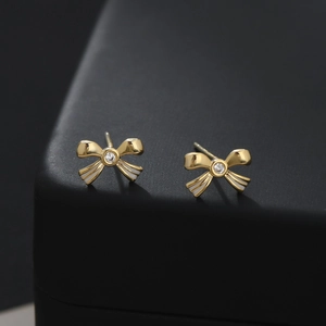 Macro shot of gold bow stud earring with white enamel stripes and a clear zircon stone