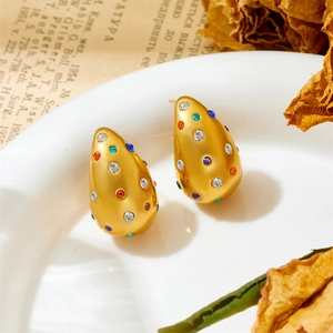 Vue macro de boucles d'oreilles gouttes dorées avec zircons colorés sur un plat blanc
