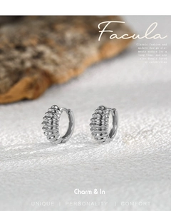 Detail of silver twisted croissant hoop earrings on white fabric with wood background