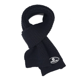 Detail of black knitted scarf featuring a teddy island logo patch and warm ribbed texture