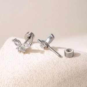 Silver butterfly screw stud earrings with light blue crystals on beige plush fabric