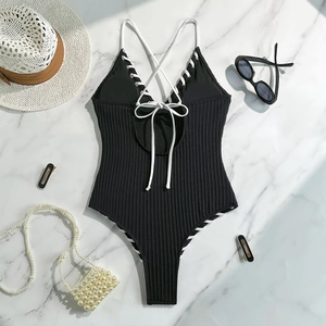 Flat lay of black ribbed one-piece swimsuit with white lace-up back and summer accessories