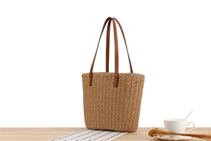 Detailaufnahme einer gewebten Papierseil-Tasche mit braunen Ledergriffen auf Holztisch