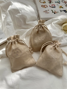 Drie beige linnen tassen met trekkoord en geborduurd smile-gezicht voor opslag