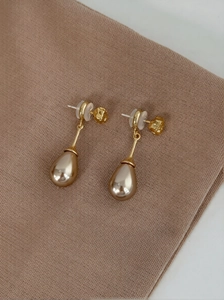 Close-up of elegant drop pearl earrings with golden finish on textured fabric