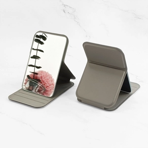 Portable folding makeup mirror with gray faux leather stand on white marble background