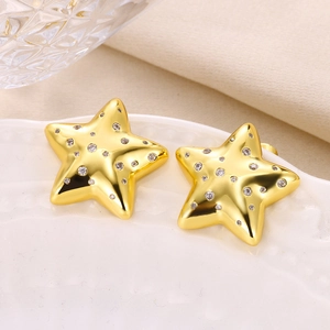 Detailed close-up of gold star stud earrings with zircon inlay on white ceramic tray