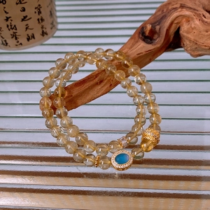 Detail of double-layer golden rutilated quartz bracelet with blue oval gemstone pendant