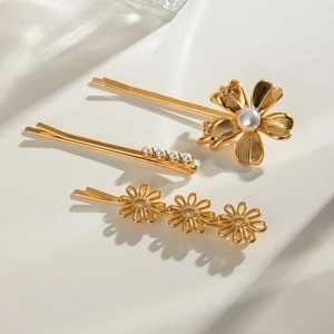 Three-piece gold metal hair clips with pearls and daisy floral designs on stone background