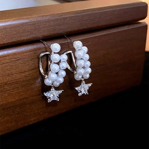Elegant pearl star drop earrings with silver metal on a wooden jewelry box edge
