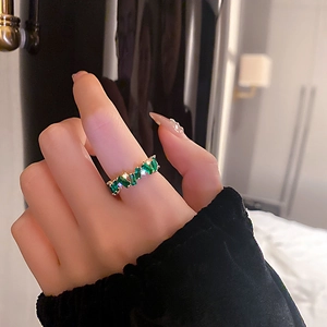 Bague élégante plaquée or avec pierres vert émeraude et zircons blancs sur une main