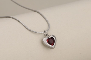 Macro shot of silver heart pendant with red faceted crystal on a sleek snake chain