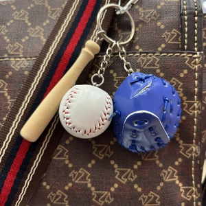 Close-up of a mini baseball keychain with wood bat and blue glove on a stylish bag