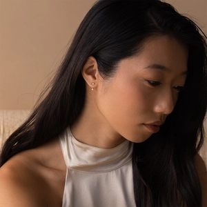 Close-up of minimalist double pearl earrings with gold base worn by a female model