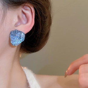 Macro view of French style irregular blue resin earrings with silver glitter texture