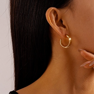 Close-up of textured gold C-shaped earrings worn by a model in a minimalist style