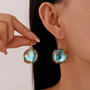 Vintage gold drop earrings with blue round resin stone and leaf motif shown on model