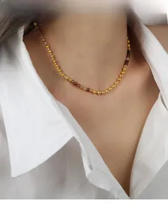 Dettaglio di collana a sfere dorate con pietre naturali marroni su modella bianca