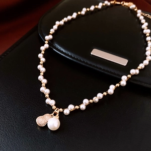 Detail of pearl necklace with gold heart pendant and lobster clasp on black leather