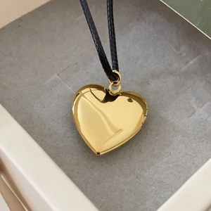Detailed view of an openable heart-shaped gold floating locket on a black cord