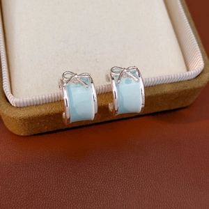 Close-up of silver C-shaped earrings with light blue enamel and a 3D bow design