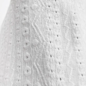 Detailed macro view of white hollow-out embroidery on cotton fabric for elegant cardigans