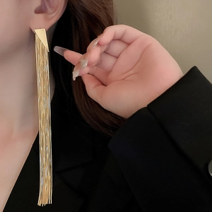 Detail of long gold tassel earrings with triangle studs worn on model side profile
