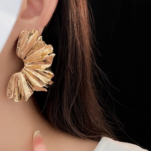 Close-up of golden pleated fan-shaped earrings worn by a model against a black background