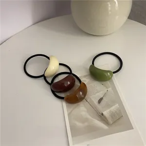 Detail of four resin hair ties in cream, brown, tortoiseshell, and green on white surface