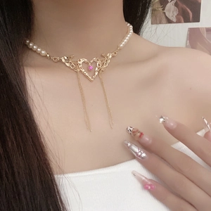 Detail of pearl necklace featuring a heart pendant with pink gem and metal tassels