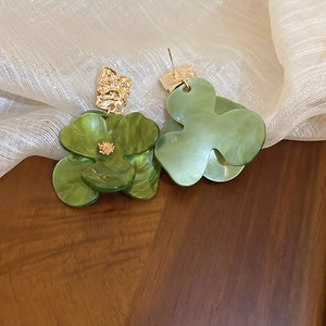 Detailed macro view of green acrylic flower earrings with textured golden metal studs