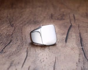 Detailed view of silver square signet ring on a dark rustic wood grain background