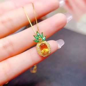 Macro shot of pineapple pendant featuring yellow gemstone and green leaves in gold