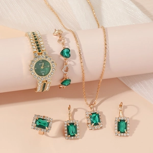 Close-up of elegant gold watch and jewelry set featuring emerald green square stones