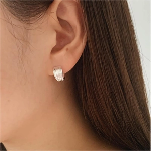 Close-up of minimalist silver huggie earrings with vertical striped texture on ear