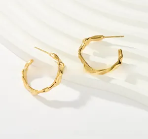Macro shot of gold-plated irregular textured C-shape hoop earrings with wavy design