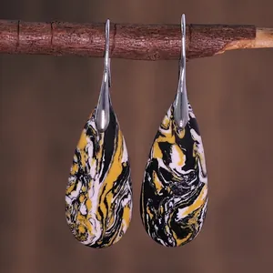 Macro shot of teardrop earrings with black and yellow marble swirls on a rustic branch