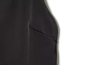Detailed close-up of fine stitching and pleated texture on black satin sleeveless top