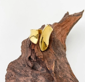 Macro shot of polished 18K gold-plated irregular open ring on dark wooden bark background