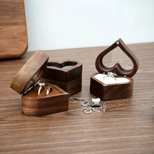 Three walnut heart-shaped wooden ring boxes with white and brown velvet inserts on wood table