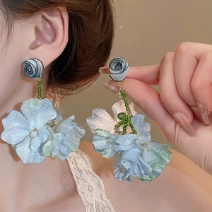 Detail of oversized floral tassel earrings with blue gradient petals and green beads