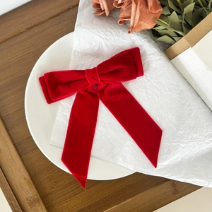 Close-up of a large red velvet bow hair clip with elegant long ribbons on white paper